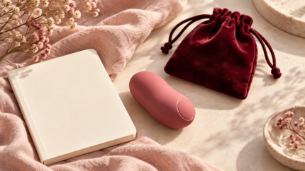 Imagen ilustrativa de un masajeador rosa, una bolsa burdeos y un cuaderno sobre lino claro